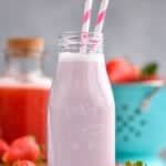 a glass bottle filled with milk next to strawberries