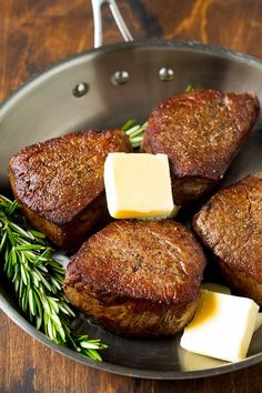 four steaks with butter and herbs in a frying pan on a wooden table