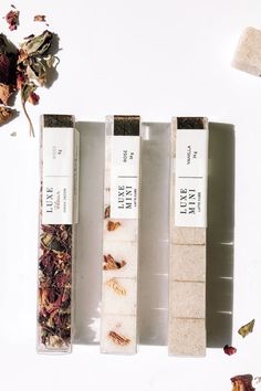 three different types of soaps sitting next to each other on a white surface with dried flowers