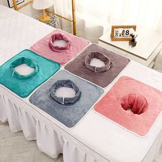 four different colored dog beds sitting on top of a bed with white sheets and pillows