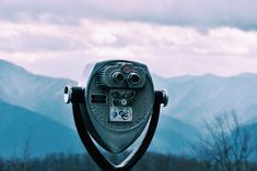 a pair of binoculars sitting on top of a metal object with mountains in the background