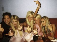 four beautiful young women sitting on top of a couch posing for the camera with their hands in the air