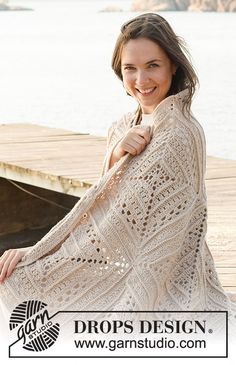 a woman is sitting on a dock wearing a crocheted shawl and smiling