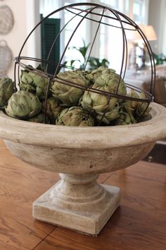 a bowl filled with green artichokes sitting on top of a wooden table