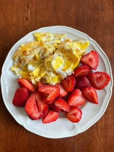 a white plate topped with eggs and strawberries on top of a wooden table next to a fork