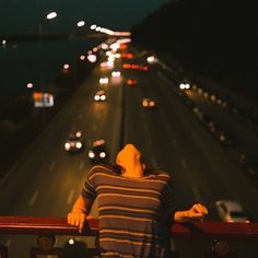 a woman leaning on a railing looking at the street lights from an overpass with cars driving down it