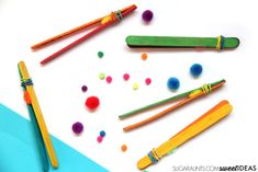 colorful pencils and colored pom - poms laid out on a white surface