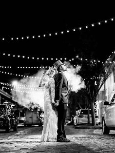 a bride and groom are standing in the street at night with lights strung above them