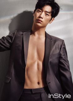 a shirtless man in a suit leaning against a wall with his hands on his hips