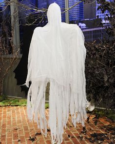 a white ghost costume on display in front of a brick floor and tree with no leaves