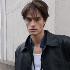 a young man wearing a black leather jacket and white t - shirt standing in front of a building