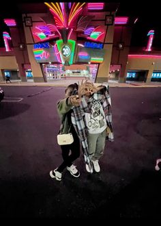 two people standing in front of a building with neon signs on the side of it