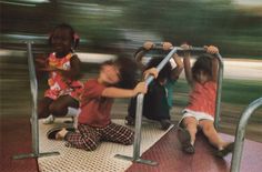 three children playing on a playground slide with their arms up and hands down, while another child holds onto the railing