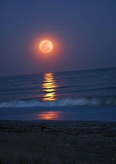 the full moon is setting over the ocean