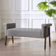 a gray bench sitting next to a potted plant on top of a hard wood floor