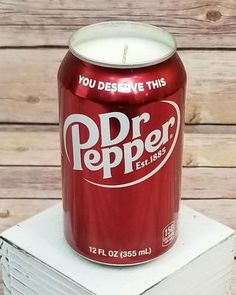 a can of dr pepper sitting on top of stack of cards with a lit candle