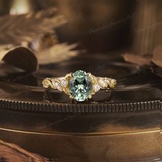 a ring with an oval green stone surrounded by leaves on top of a wooden surface