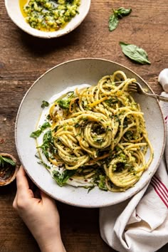 someone is holding a plate of pasta with pesto and parsley on the side