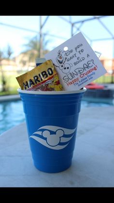 a blue cup filled with candy and some kind of card on top of a table next to a swimming pool