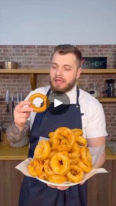 a man in an apron holding a plate with onion rings