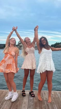 three girls standing on a dock with their arms in the air