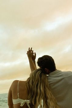 a man and woman sitting on the beach with their arms in the air looking out at the ocean