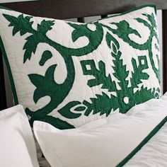 a green and white quilted pillow sitting on top of a bed next to pillows