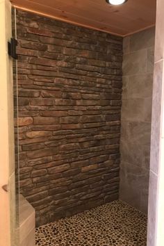 a walk in shower sitting next to a stone wall and tiled floor with a light above it