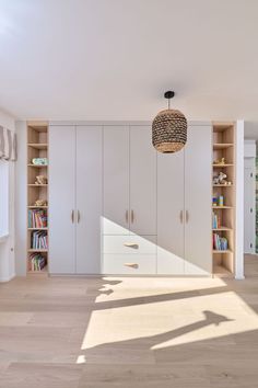 an empty room with white cabinets and wooden floors is pictured in this image, the light shines on the bookshelves