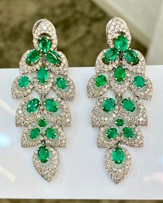 These Designer vintage style Dangle Emerald earrings from the Retro era are crafted in solid 18k white gold. They expose each an enchanting EMERALD from Zambia, cumulatively weighing 7.13carats. The transparent precious gemstones are secured by multiple prongs and surrounded by diamond perimeters, a slender diamond-studded profile. These earrings are collectively adorned with genuine round-faceted diamonds weighing approx. 5.17carats graded F color and VS clarity. Featuring posts and clasps, the earrings are designed for pierced ears exclusively. These stunning retro earrings with a captivating aesthetic are in excellent condition, is brand new and ready to ship.   The Emerald are Bright, Vibrant, Open Green Hue with Vivid Saturation, a Medium Tone, and Subtle  Greenish blue Undertones. Th Luxury Pierced Chandelier Earrings For Formal Events, Luxury Pierced Chandelier Earrings For Anniversary, Luxury White Gold Pierced Bridal Earrings, Luxury Green Chandelier Earrings, Green Sterling Silver Luxury Diamond Earrings, Luxury Green Sterling Silver Diamond Earrings, Luxury Green Diamond Earrings In Sterling Silver, Luxury Oval White Gold Bridal Earrings, Luxury White Gold Chandelier Earrings With Prong Setting