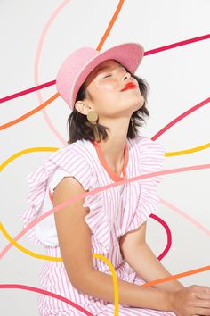 a woman wearing a pink hat sitting on top of a white floor next to a wall