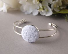 a close up of a bracelet on a table with flowers in the background and a white flower