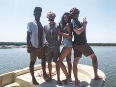 four people standing on the edge of a boat in the water, posing for a photo