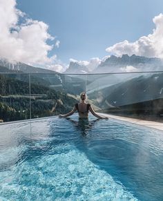 a woman is sitting in the middle of a swimming pool with mountains in the background