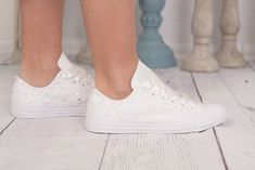 a woman's legs wearing white sneakers with sequins on them, standing in front of a table