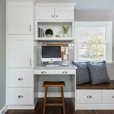 a home office with built - in desk and storage cabinets, along with two stools