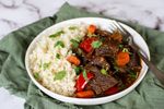 a white bowl filled with beef and rice on top of a green cloth next to a fork