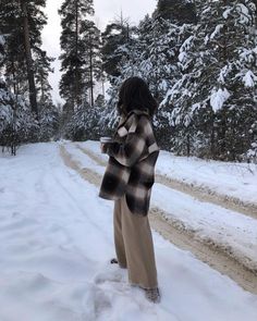 a woman standing in the middle of a snow covered road wearing a coat and pants