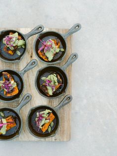 six cast iron skillets filled with food on top of a wooden cutting board next to utensils