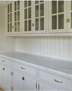 a kitchen with white cabinets and marble counter tops, gold pulls on the cupboards