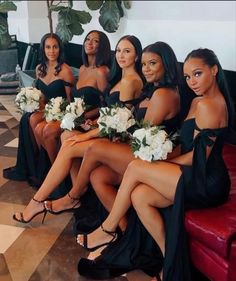 four beautiful women in black dresses sitting on a red couch with white flowers and greenery