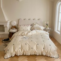 a bed with white sheets and pillows in a bedroom next to a window on a hard wood floor