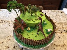 a dinosaur themed cake on top of a kitchen counter with green frosting and trees