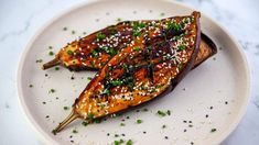 two grilled carrots on a white plate topped with sesame seeds and seasoning