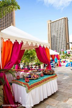 a table with some food on it under a white and orange tent in the middle of a city