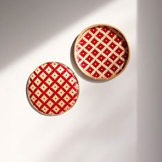 two red and white cross - stitched buttons sitting next to each other on a white surface