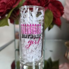 a birthday girl glass with pink candles and white shredded paper in the bottom is surrounded by red roses