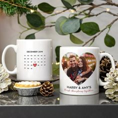 two personalized coffee mugs on a table with pine cones and greenery in the background