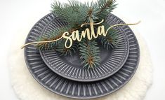 a plate that has some pine branches on top of it with the word santa spelled in gold