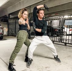 a man and woman standing in front of a car with their hands up to the side